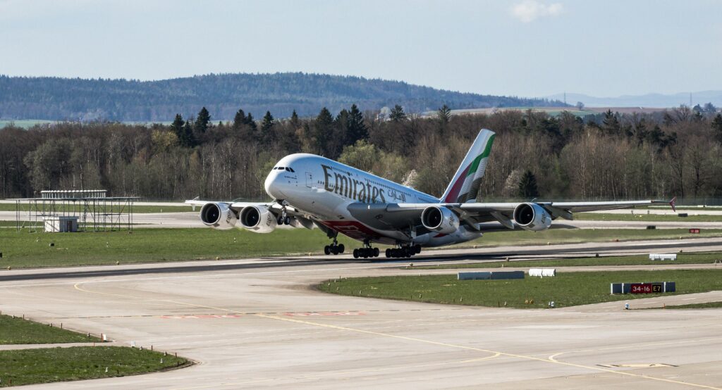 Emirates Airbus A380 taking off in daylight at Zurich Airport with scenic backdrop.