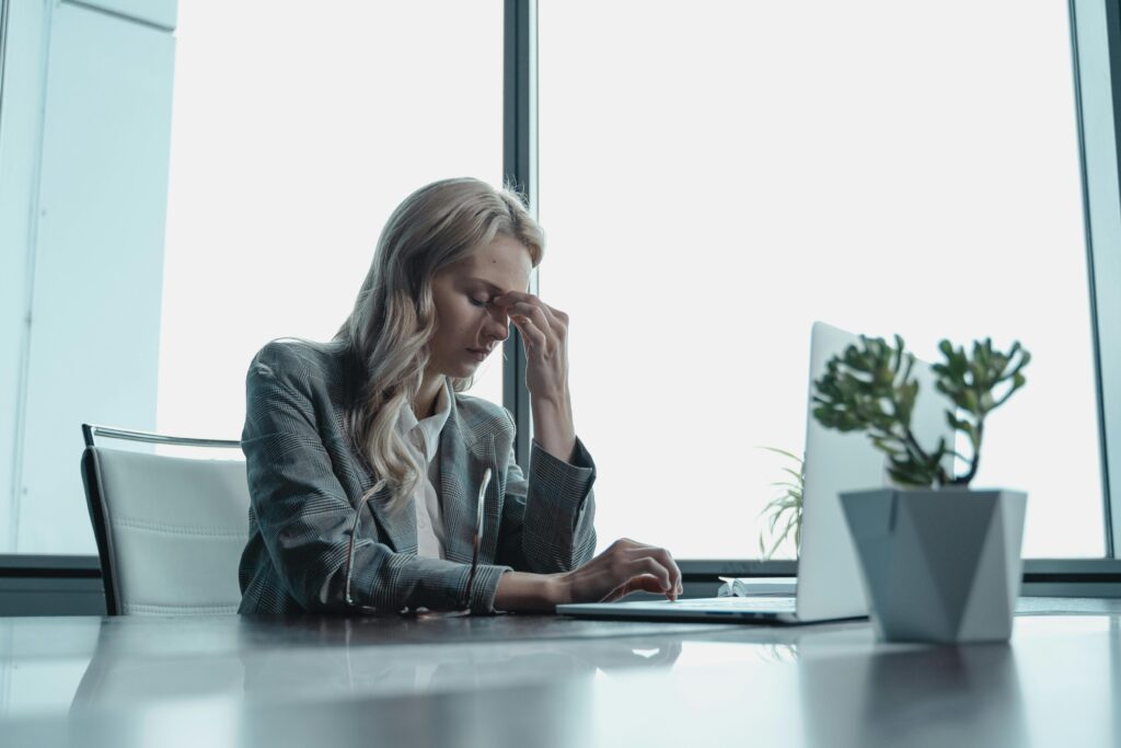Professional woman in office, sitting at desk, looking stressed with laptop.