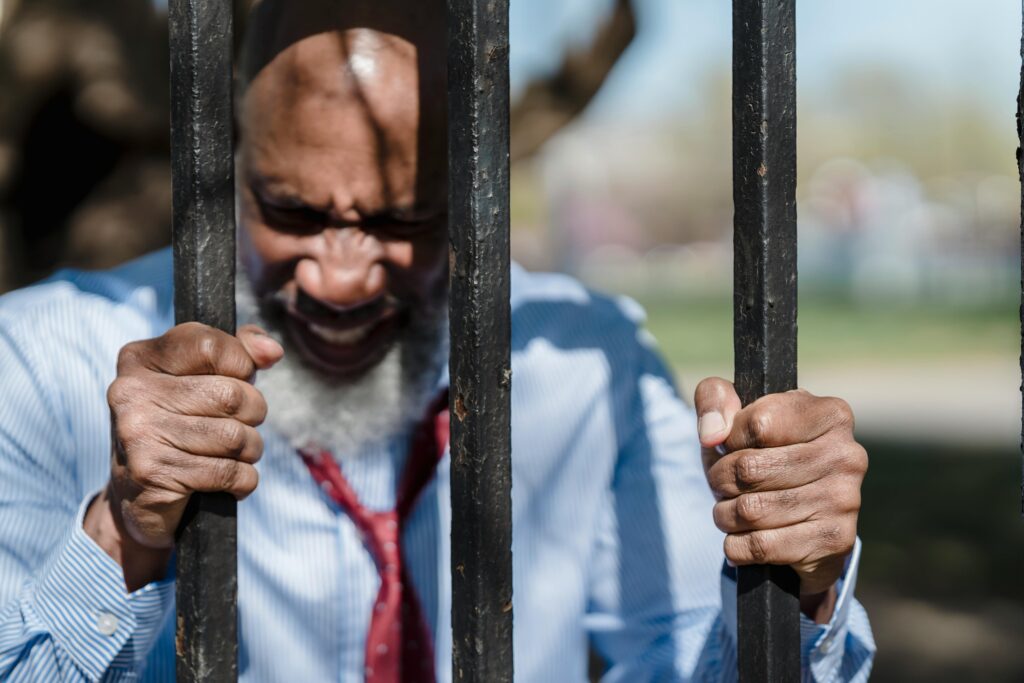 A frustrated man gripping metal bars outdoors, expressing anger and determination.