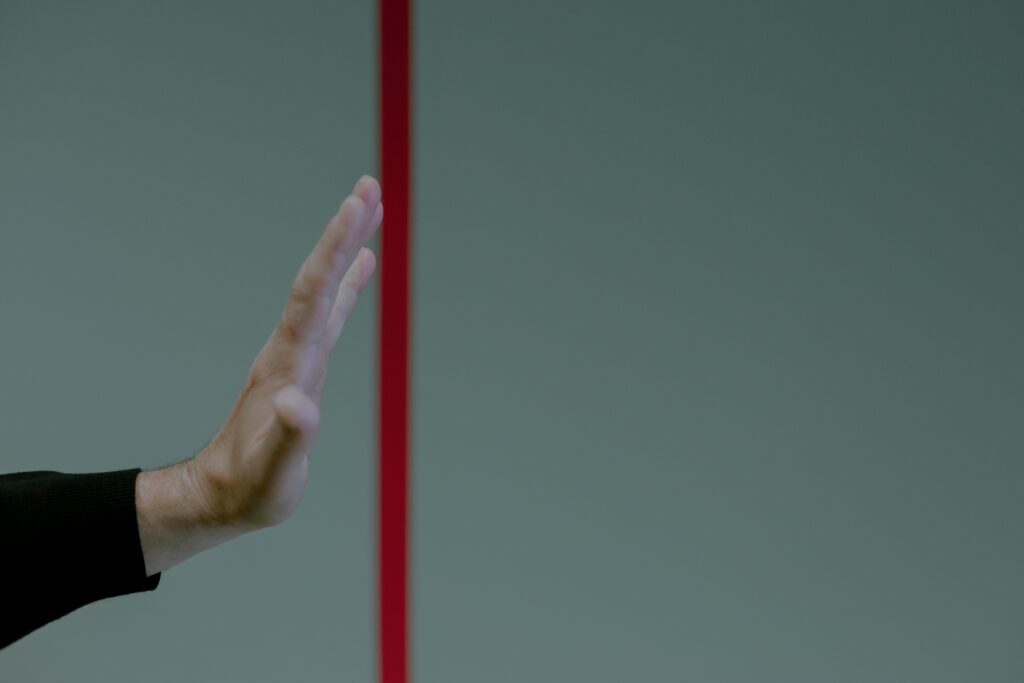 Close-up of a man's hand gesturing stop in front of a vertical red line, concept of boundary.